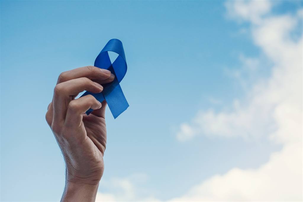 Mão masculina segurando o laço azul do Novembro Azul contra o céu